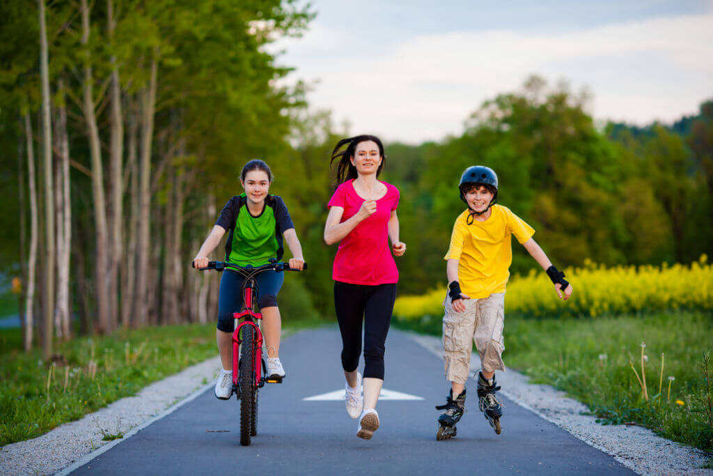 woman running with girl on bike and boy on roller blades