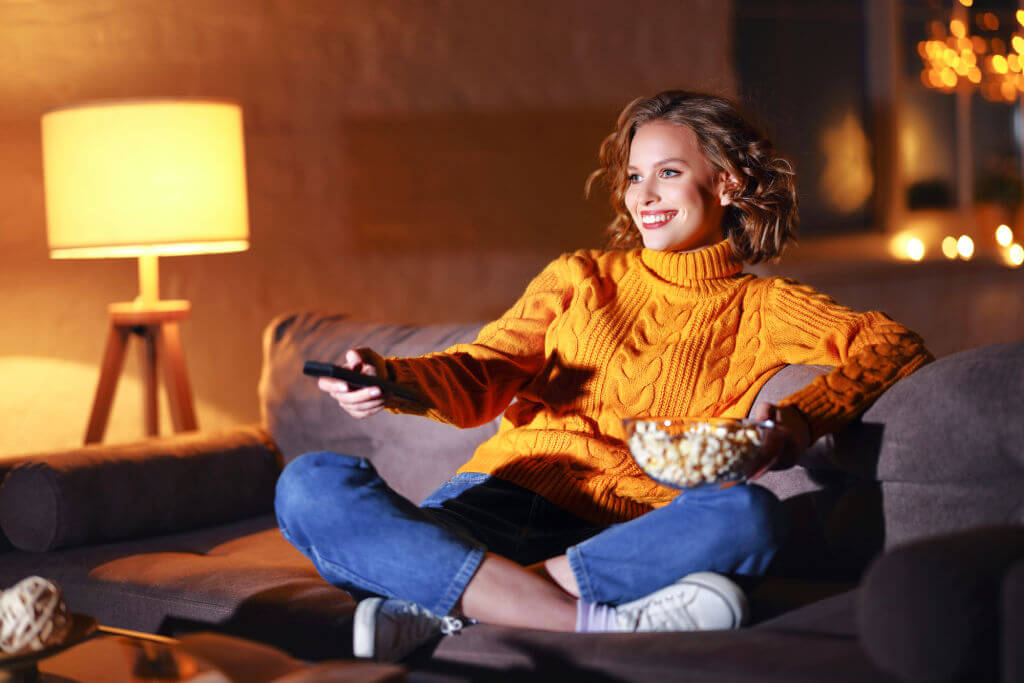 woman watching tv with a remote and popcorn, with lights in the background