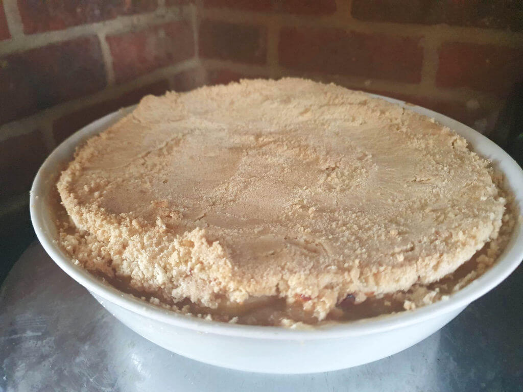 apple crumble in a white round dish against brick background